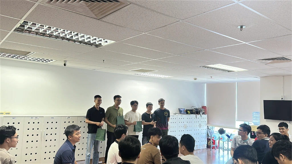 A group of people standing at the front of a room while others sit and watch during an office gathering